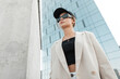 © alones - Beautiful fashionable urban woman with stylish sunglasses and a black cap in fashion casual clothes with a blazer and top walks in the city