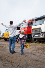 man and kid, holding hands, stand with their backs, look at construction site, where excavators with large buckets are located. Son's passion for construction equipment. Interesting excursions for boy