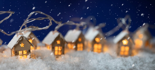 Leinwandbilder - Abstract Christmas Winter Panorama with Wooden Houses Christmas String Lights in Cold Snow Landscape and Glowing Golden Lights in Background. Panorama, Banner. Christmas or Energy themes.