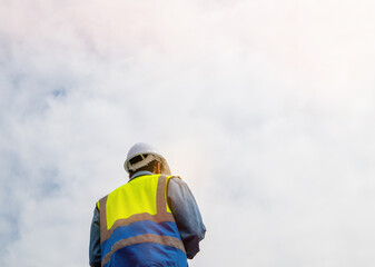 Rear view of positive worker in safety helmet against blue sky. Use as copy space, banner or background.