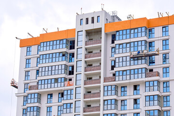 Wall Mural - Worker in suspended platform paint facade, construction cradle hanging on ewsidential building plastering work. Finishing facade work. Construction worker working at height in lifting platform