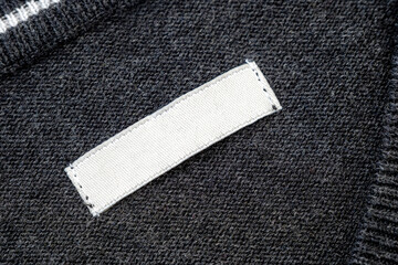 White blank label, patch or tag with space for text  on knitted gray sweater, top view