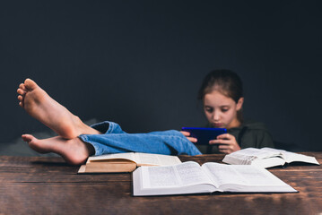 a girl with a phone in her hands. the girl plays on the phone, ignoring books and studies. open book