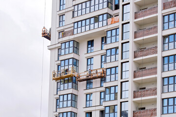 Wall Mural - Workers in lift platform caulk, seal exterior glass window, maintain exterior glass facade. Men in lifting platform at height insulate and seal around building windows. Worker in suspended platform