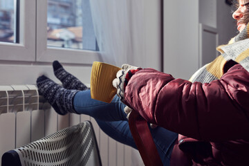 Wall Mural - Woman in jacket, scarf and hand gloves indoors on a chilly winter day, energy and gas crisis, cold room, heating problems.