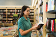 © AntonioDiaz - Smiling hispanic woman looking to buy a new book at the store