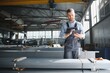 © Serhii - Portrait of factory worker in protective uniform and hardhat standing by industrial machine at production line. People working in industry