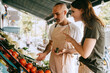 © Maskot - Side view of female customer gesturing while talking to male vendor holding vegetable at market