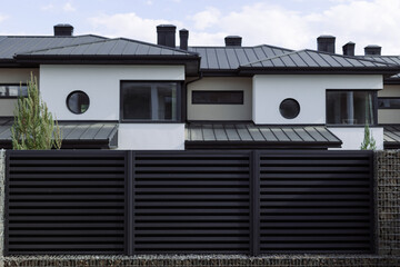 New cottages with a metal black fence on a blue sky background