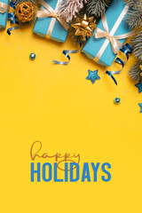 Wall Mural - Happy Holidays text on yellow background with pine tree, blue gifts and festive decorations top view. Xmas greeting card