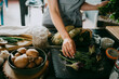 © Maskot - Female chef arranging broccolini and aubergines on slate at counter in studio kitchen