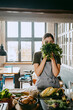 © Maskot - Young female chef smelling fresh cilantro standing in studio kitchen