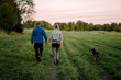 © Maskot - Mature couple holding hands and walking with dog on field during sunset