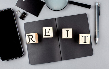 Wall Mural - Word REIT on wooden block on black notebook with smartpone, credit card and magnifier