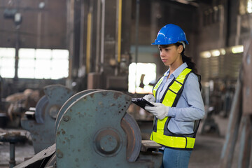 Wall Mural - Woman worker checking or maintaining machine at the industry factory area. Female worker wear safety helmet and uniform working in the factory