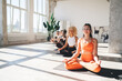 © BullRun - Ethnic woman meditating in lotus pose in gym with friends