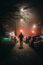Man Walking Alone Down A City Street Sidewalk On A Foggy Night.