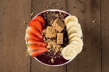 White Bowl of Brazilian Frozen Açai Berry With Paçoca, Strawberry and Banana. on a wooden desk. Top view