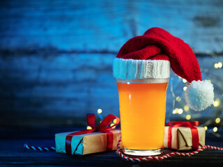 Festive Christmas beer glass in a knitted Santa hat and gift boxes with red ribbons on a blue background. Copy space