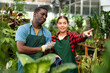 © JackF - Young confident woman horticulturist in an apron is discussing something with an African american man colleague during work in a flower greenhouse