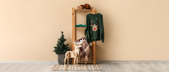 Shelving unit with sweater, clothes, wooden reindeer and Christmas tree near beige wall in room