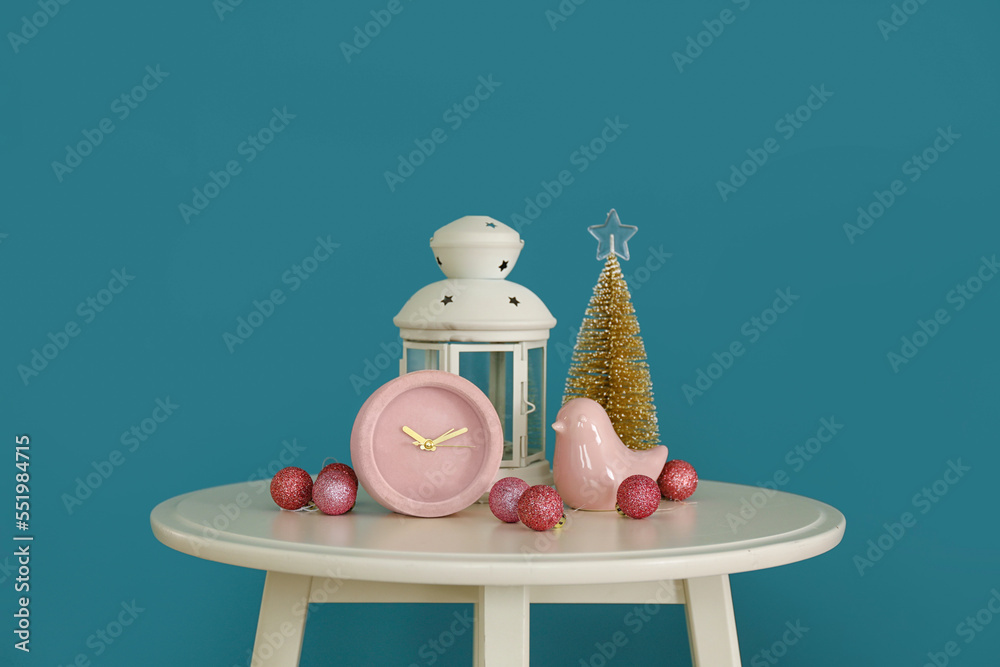 Alarm clock with Christmas decor and lantern on table near blue wall