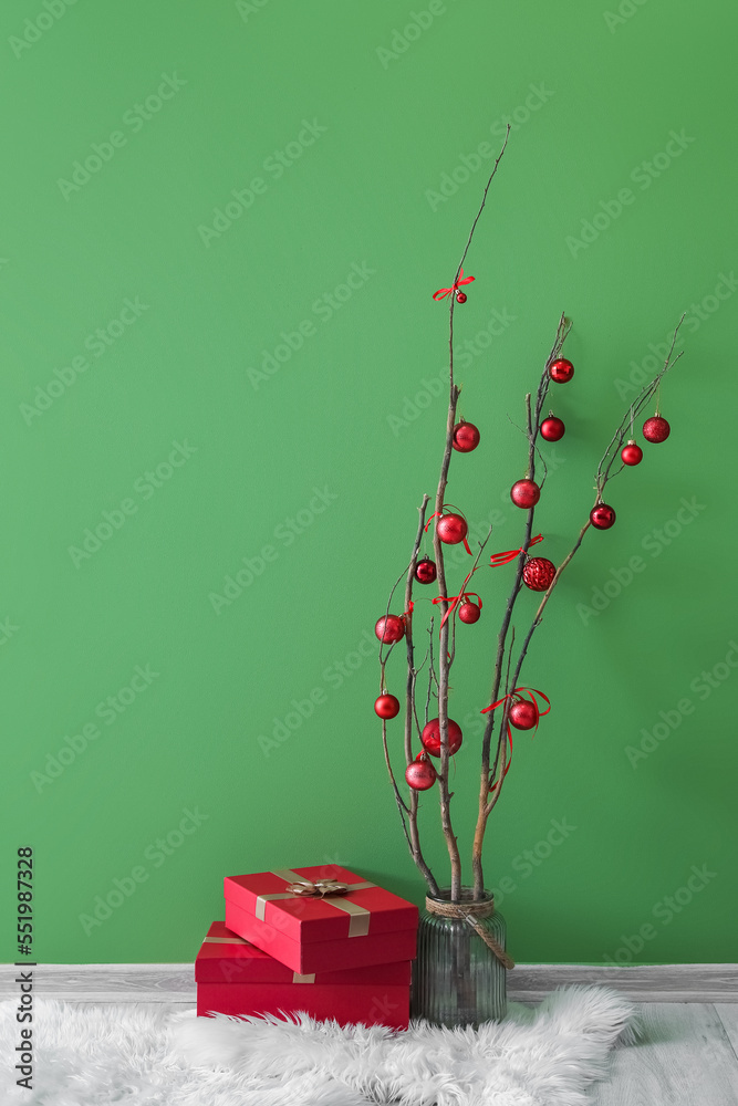 Vase with tree branches, Christmas balls and presents on rug near green wall
