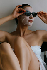 Wall Mural - Young beautiful woman is resting in white fabric mask on her face and wearing black sunglasses