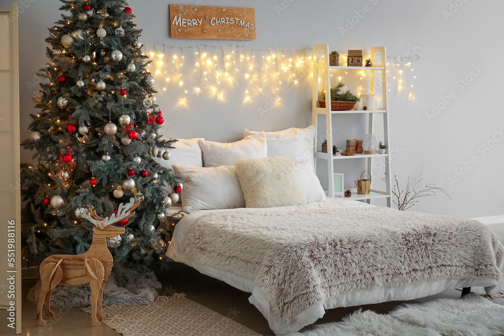 Interior of bedroom with Christmas tree, glowing lights and shelving unit