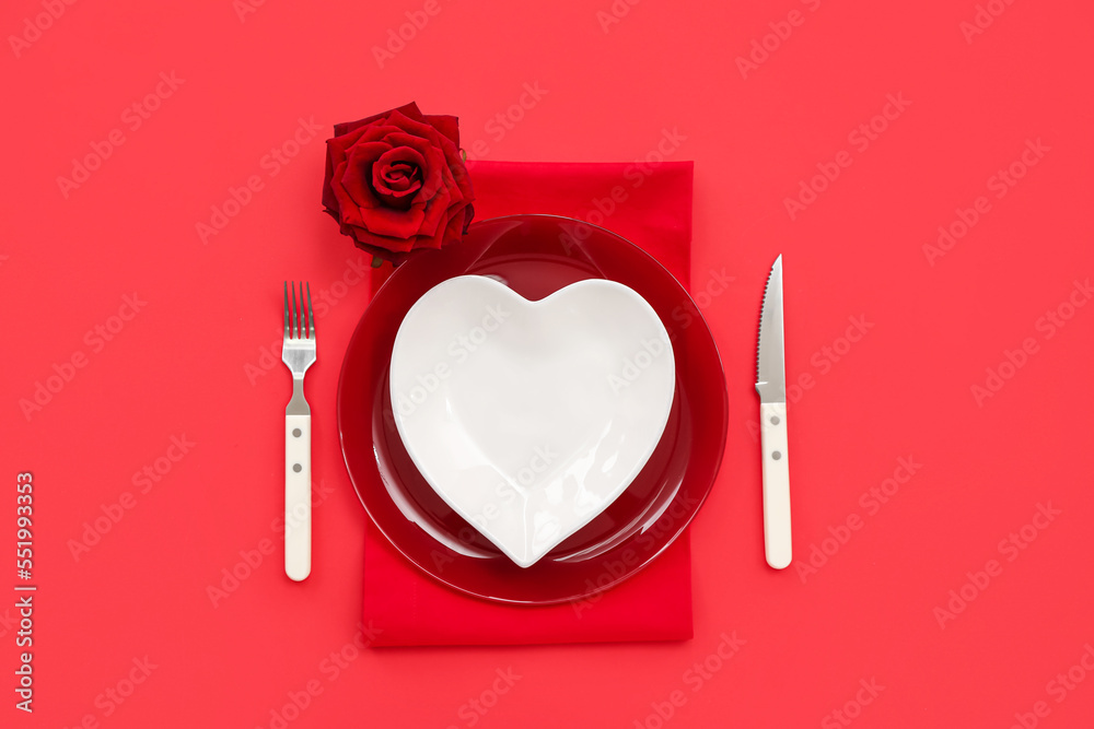 Table setting for Valentine's Day with heart shaped plate and rose on red background