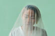 © Clique Images - Horizontal close up portrait of sorrowful young woman under tulle on pale cyan background