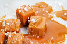 Salted caramel, a taste sensation. Coarse salt and caramel blocks covered in a sticky creamy salted caramel sauce on grey