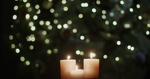 Three Candles Burn Against The Backdrop Of Blurry Christmas Tree Lights.