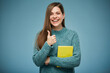 Smiling woman holding yellow book showing thumb up. Isolated advertising portrait.