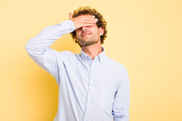 Wall Mural - Young smart caucasian man on yellow background covers eyes with hands, smiles broadly waiting for a surprise.