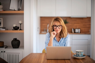 Wall Mural - Beautiful mid aged woman using laptop while working from home. Home office. 