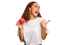 Young Caucasian Woman Holding A Red Apple Isolated Points With Thumb Finger Away, Laughing And Carefree.