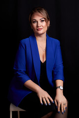 Wall Mural - caucasian adult woman sitting in a blue jacket on a chair on a black background