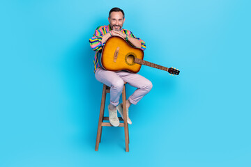 Poster - Photo of positive talented eccentric showman host sitting stool preparing concert isolated on blue color background