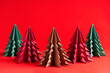 Group of handmade crafted christmas fir trees origami made of folded paper of different colours on bright red background prepared for celebration of new year holiday. Alternative life concept