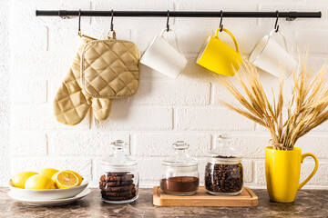 Wall Mural - front view of the kitchen marble countertop with cans of coffee and a bowl of lemons. kitchen rail with mugs on a white brick wall.