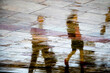 Abstract blurry silhouette reflections of unrecognizable people walking on wet city street pavement on a rainy day
