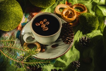 Wall Mural - Still life- a cup of hot coffee and roasted beans. Breakfast mug on a dark green background- table is decorated with sprigs of spruce.