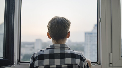 Back view of teen boy looking through window, sad orphan kid waiting on adoption