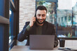 © atitaph - portrait of a successful business man Working on a laptop computer and using a smartphone to work in a coffee shop.