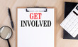 GET INVOLVED text on a clipboard on wooden background