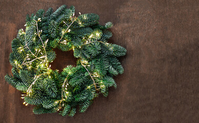 Wall Mural - christmas tree branches with golden lights garland on dark wooden background. xmas, nature new year 