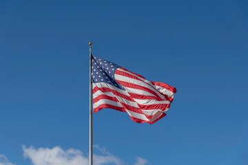 A large American flag blows in the wind against a bright blue sky.