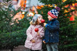 Two little smiling kids, boy and girl eating crystalized sugared apple on German Christmas market. Happy friends in winter clothes with lights on background. Family, tradition, holiday concept