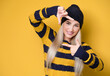Woman shows frame with her fingers. Attractive girl set up definition, model wearing woolen cap and sweater, isolated on yellow background. Focus on face